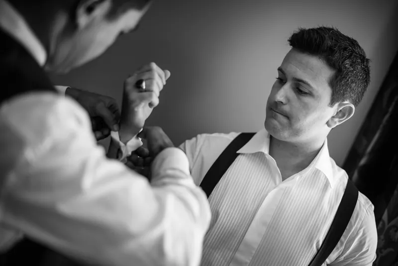 A groomsman carefully fastens Michael's cufflink in black and white.