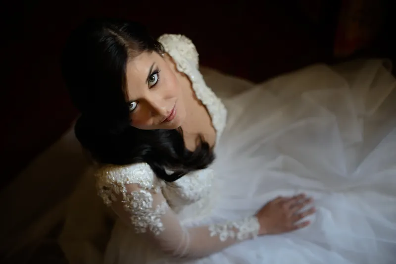 Choko leans back on white fabric, beaded bodice catching light as she gazes toward the camera.