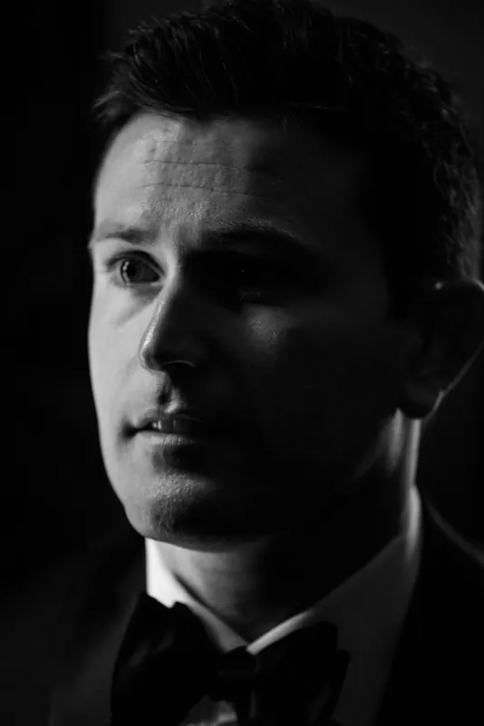 Michael's profile emerges from shadow, sharp jawline and dark hair framed in dramatic black-and-white lighting.