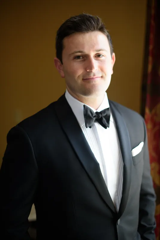 Michael stands in a gray suit and bow tie, offering a composed smile against a warm golden background.