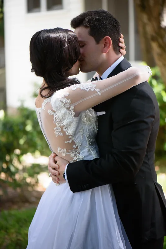 Choko and Michael kiss beneath tree-lined grounds with white columns visible behind them.