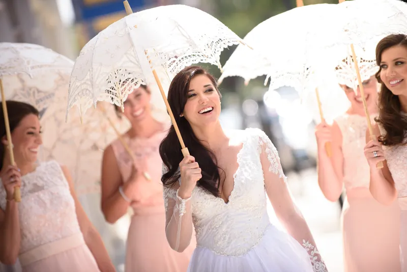 Choko and three bridesmaids hold delicate lace parasols, smiling and laughing together on a sunny street.