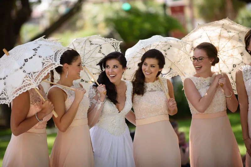 Four bridesmaids huddle beneath ornate lace umbrellas, laughing and posing together in Downtown St Augustine.