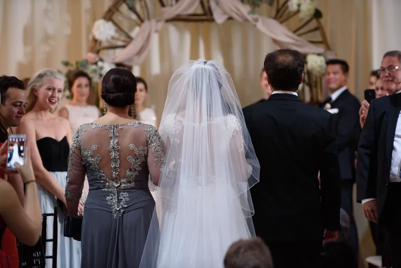 Choko in her lace veil stands between Michael and a bridesmaid as guests watch the ceremony unfold at The Treasury