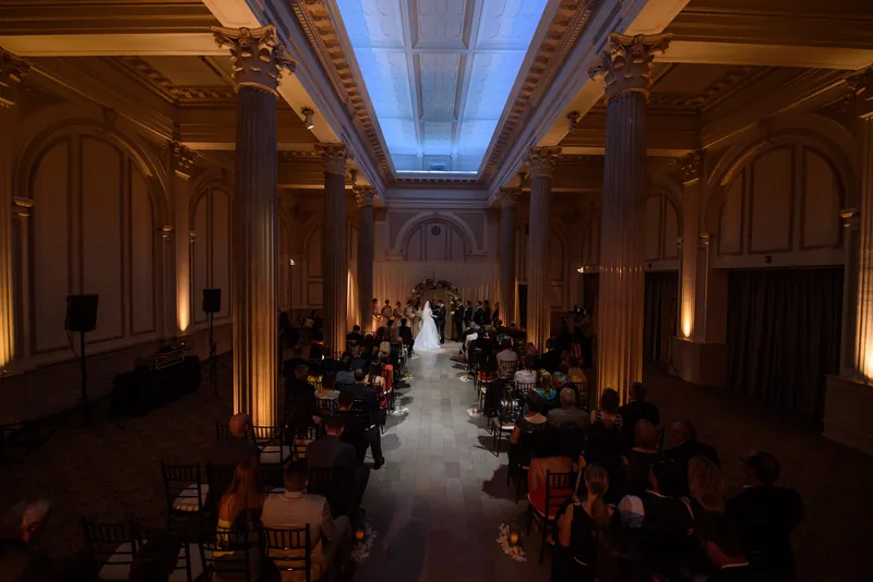 The grand ceremony hall at The Treasury on the Plaza glows with golden uplighting as rows of guests witness Choko