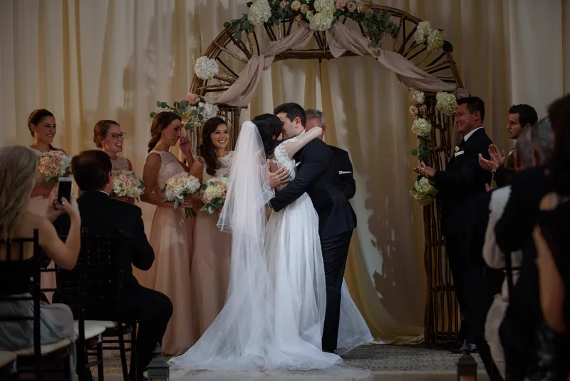 Michael and Choko exchange vows beneath a floral arch at The Treasury on the Plaza with their wedding party surrounding them.