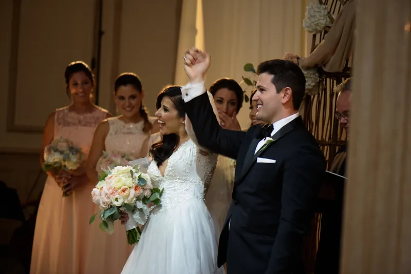 Michael raises Choko's hand triumphantly moments after their ceremony as bridesmaids smile from the side.