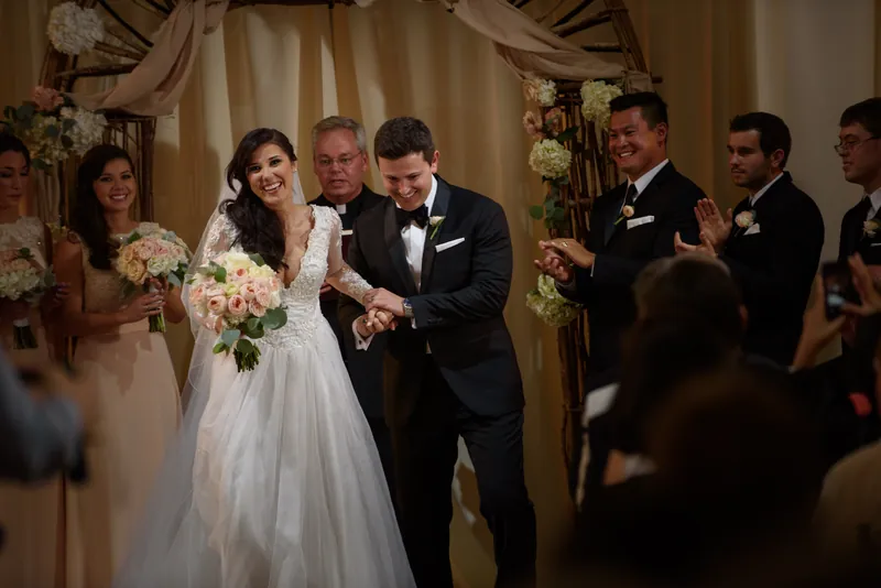 Choko and Michael laugh together during their recessional while guests in formal attire celebrate around them.