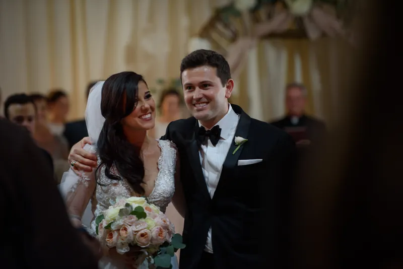 Choko and Michael gaze at each other with warm smiles, newlywed and radiant, surrounded by blurred guests in the background.