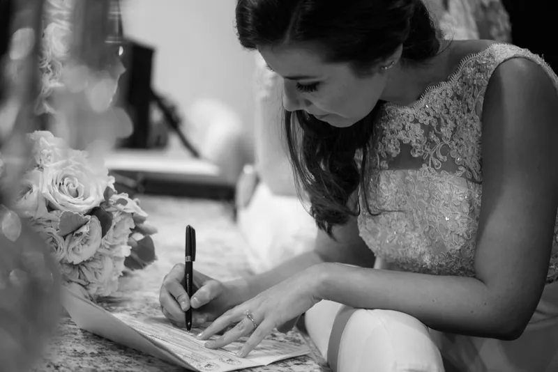 Choko signs the marriage certificate in black and white, her face concentrated as she completes the official paperwork.