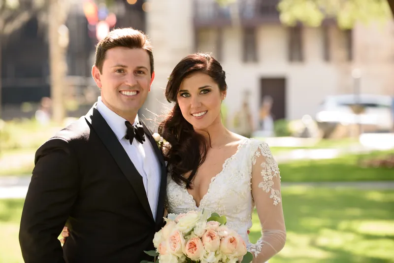 Michael and Choko smile for a portrait holding her bouquet downtown, dressed in formal wedding attire.