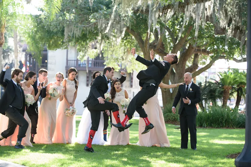 Michael and a groomsman leap into the air while Choko and wedding guests watch on the shaded lawn in Downtown St Augustine.