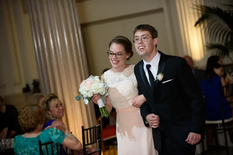 Michael and Choko walk down an interior hallway at The Treasury on the Plaza, Choko carrying a white bridal bouquet.