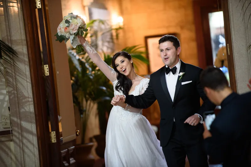 Choko raises her bouquet joyfully while Michael smiles beside her in the elegant corridors of The Treasury on the Plaza.