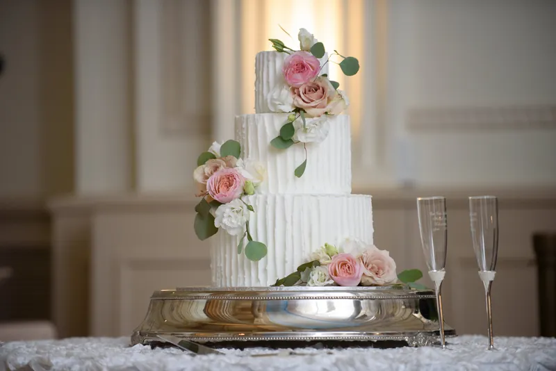 Three-tiered white cake adorned with pink roses and eucalyptus leaves sits on a gold-trimmed table at The Treasury