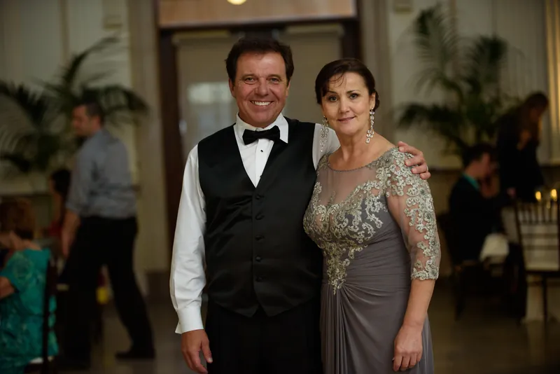 Michael in a black vest and bow tie stands with Choko, who wears a beaded gray gown, at their reception.