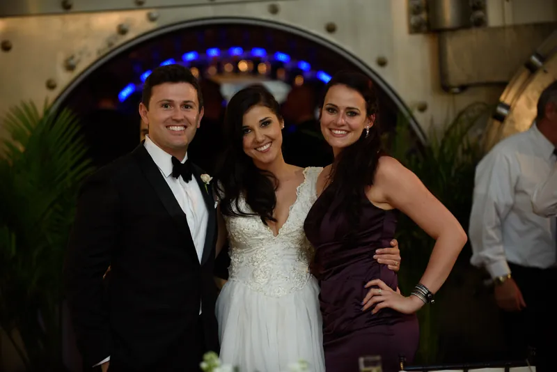 Michael, Choko in a beaded white dress, and a guest pose together under blue uplighting at the venue.