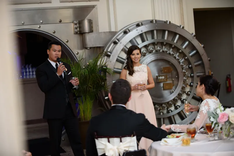 Michael addresses guests at the reception while Choko listens in her white lace gown beside a distinctive spiral staircase.