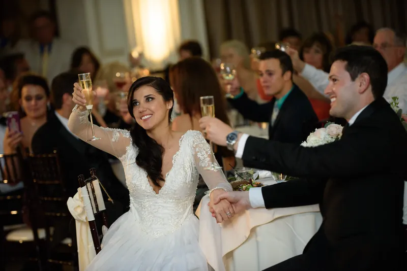 Choko raises her champagne glass in a toast, flanked by guests in formal attire at the reception.