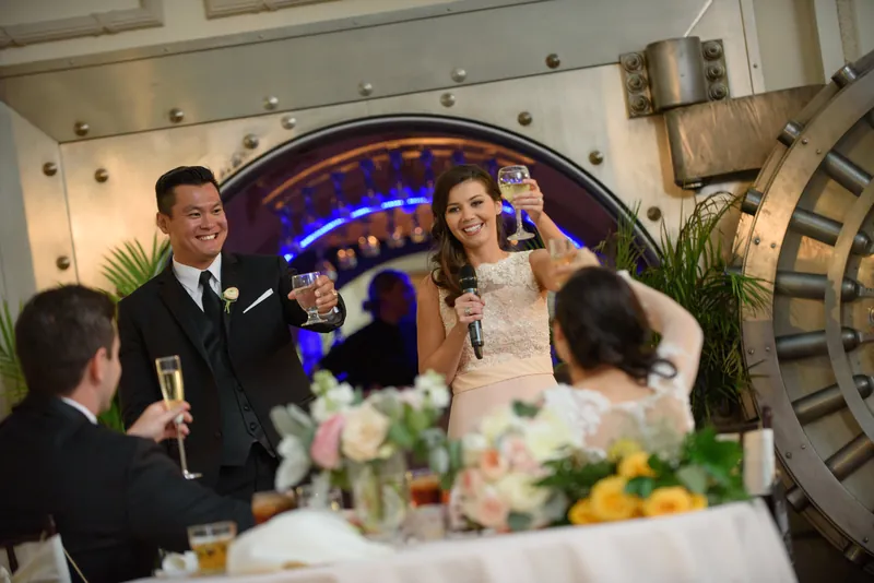 Michael and Choko raise their glasses in a toast before the illuminated vault, with wedding guests gathered around