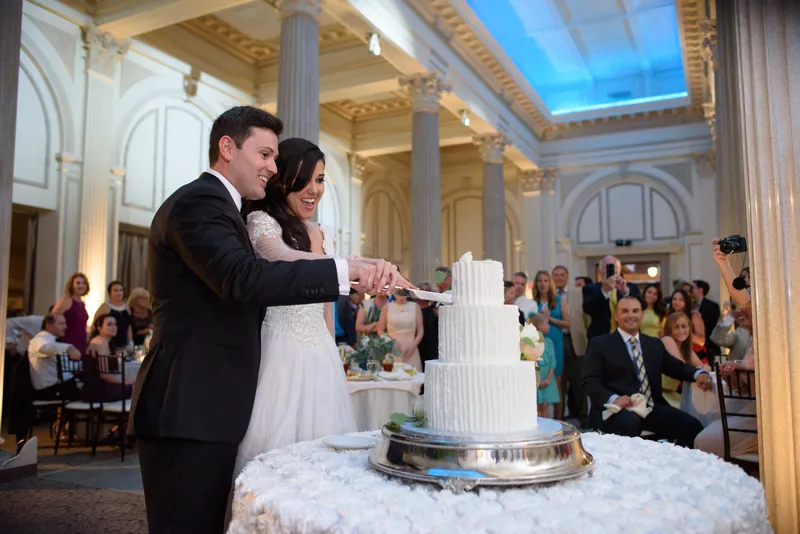 Michael and Choko cut their tiered wedding cake together in the grand ballroom surrounded by standing guests and ornate