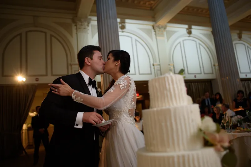 Michael and Choko kiss beneath soaring columns and classical architecture as their reception guests look on.