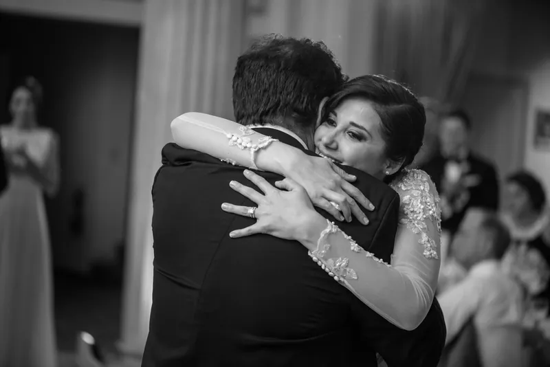 Choko embraces a guest in black and white, her beaded dress catching light as she hugs them warmly.