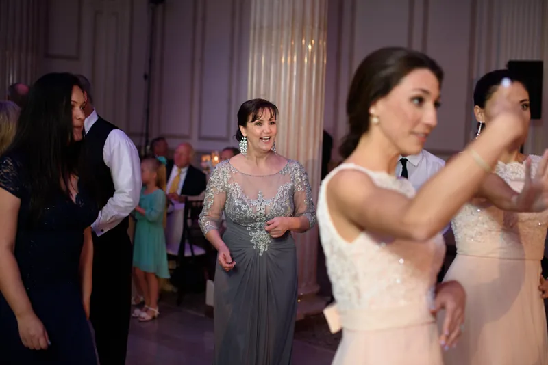 Choko dances with guests at The Treasury on the Plaza while wearing her white wedding dress among purple-lit celebration.