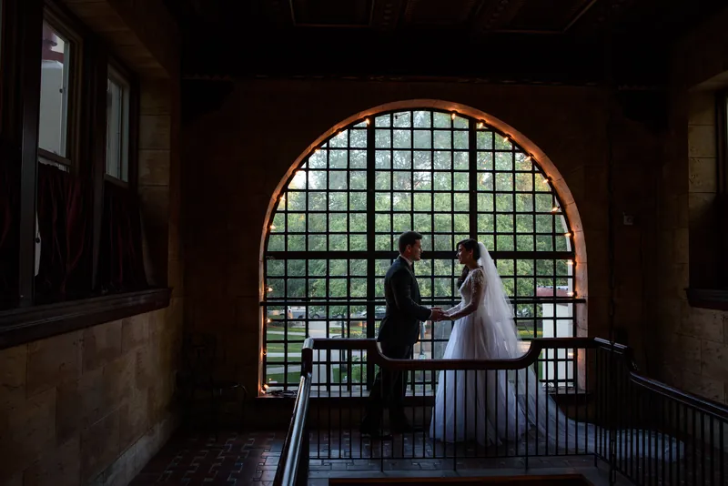 Choko and Michael stand together framed by an arched doorway with gridded windows at The Treasury on the Plaza.