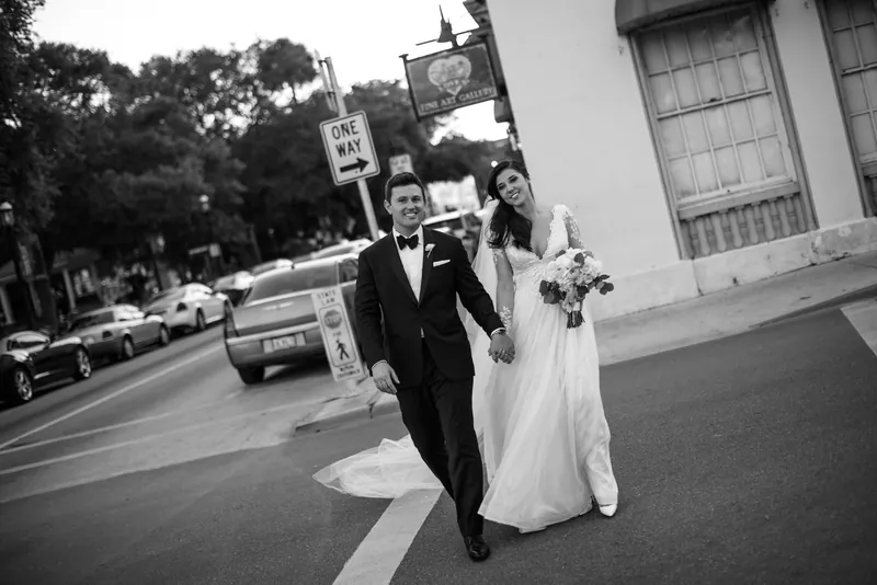 Michael and Choko walk down a downtown St. Augustine street in formal wedding attire, her veil trailing behind them.
