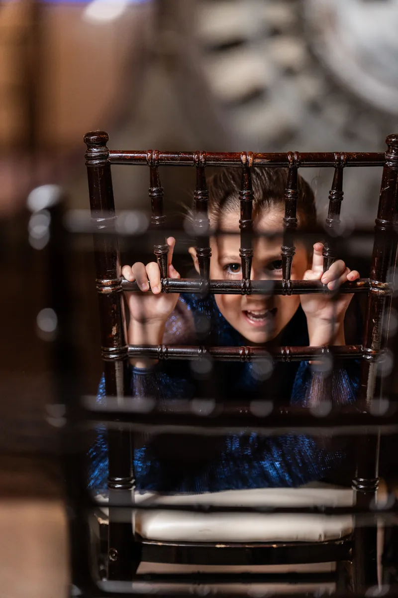 Young girl peeking playfully through chiavari chair bars at The Treasury venue