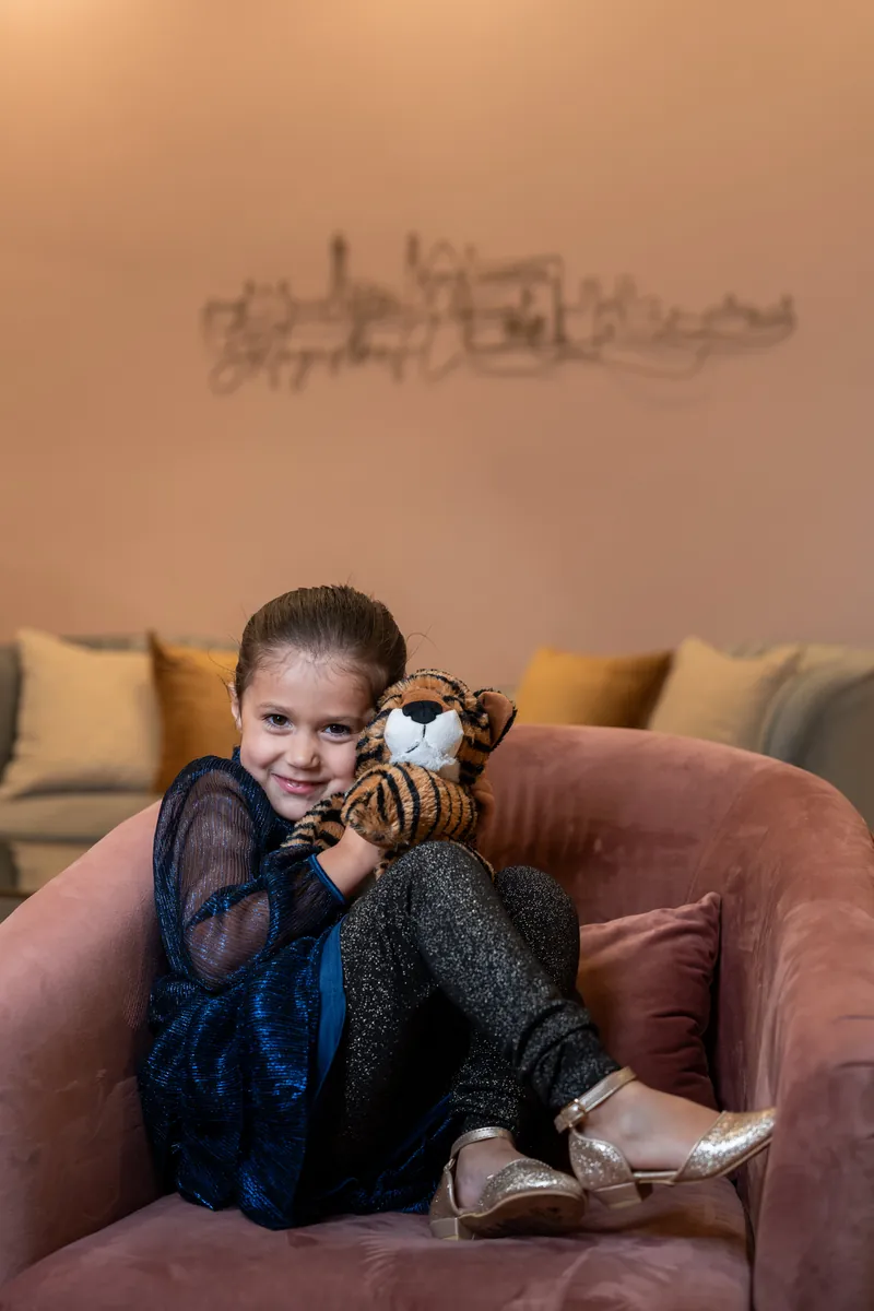 Little girl sitting on pink velvet couch hugging stuffed tiger toy
