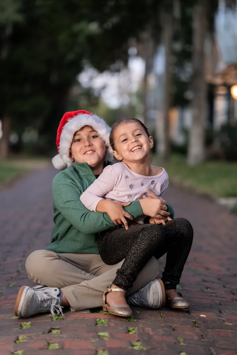 Siblings hugging on brick street with Santa hat during holiday session