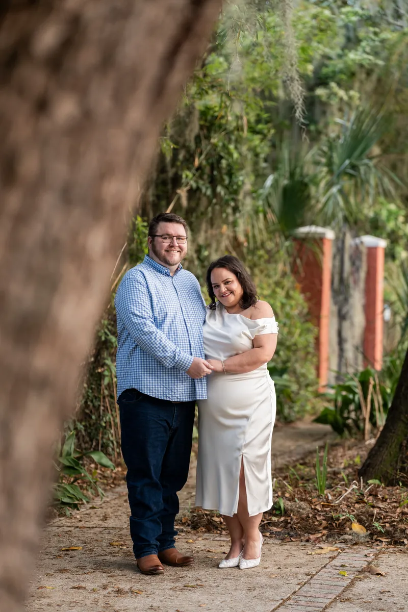 Chris and Shelby stand close together on a brick pathway surrounded by ivy-covered walls and green foliage.