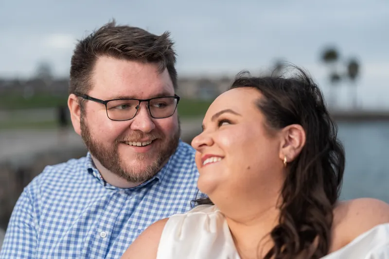 Chris and Shelby smile at each other outdoors with a waterway and palm trees visible behind them on an overcast day.