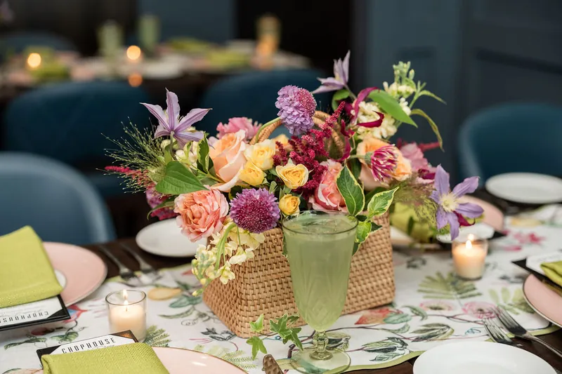 Pink and yellow roses with burgundy dahlias arranged in a woven vase at Chophouse at Nocatee, with candlelit place settings