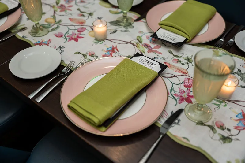 Table setting at Chophouse at Nocatee with white plates, pink chargers, olive-green napkins, and a floral table runner