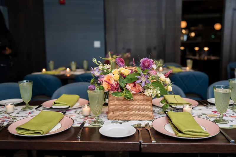 Full table view at Chophouse at Nocatee showing three place settings with pink chargers, green napkins, and a central floral
