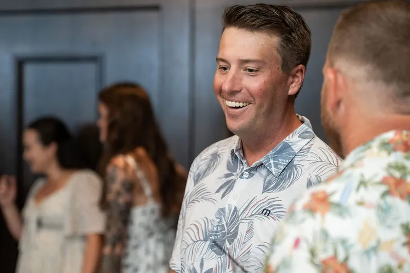 A man in a patterned shirt laughs while chatting with guests at the event.