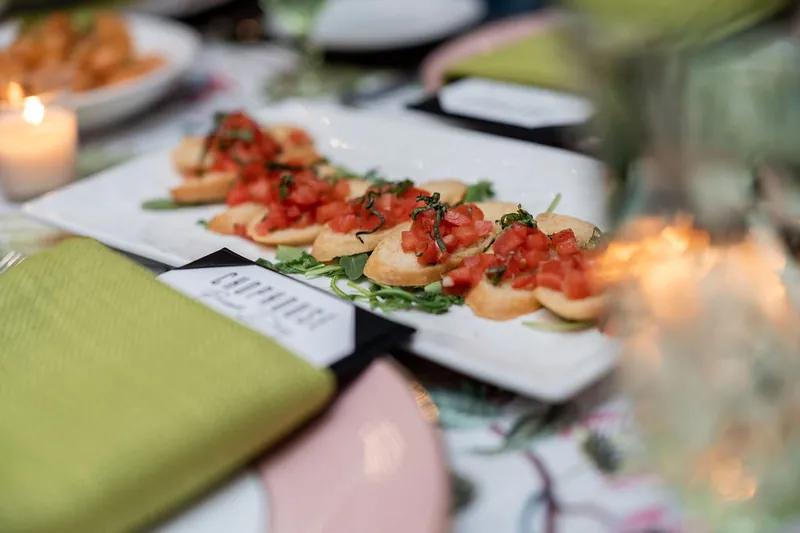Plated appetizers with tomato topping line a white plate at a candlelit dining table.