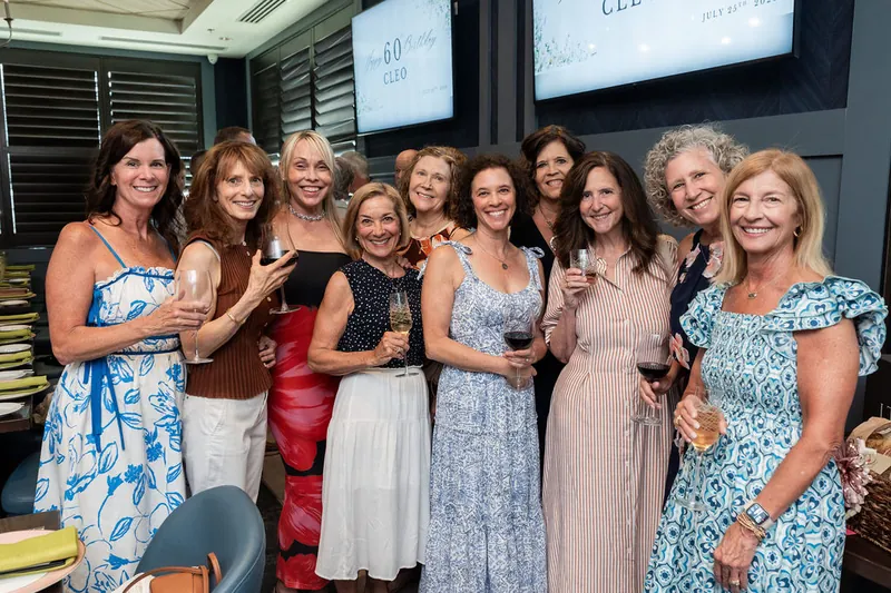 Eleven women in varied pastel and patterned dresses stand together smiling indoors at Chophouse at Nocatee.