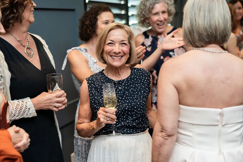 Women in a navy polka-dot top and white skirt smile broadly while chatting with guests at the celebration.