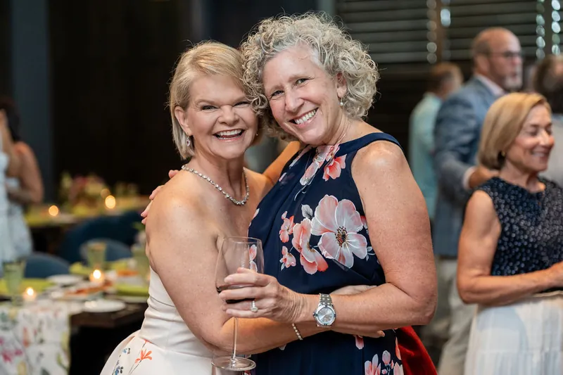 Two women in sleeveless dresses embrace while holding beverages at Chophouse at Nocatee's event space.