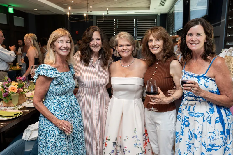 Five women smile together at Chophouse at Nocatee, dressed in patterned and solid pastels, holding drinks and posing