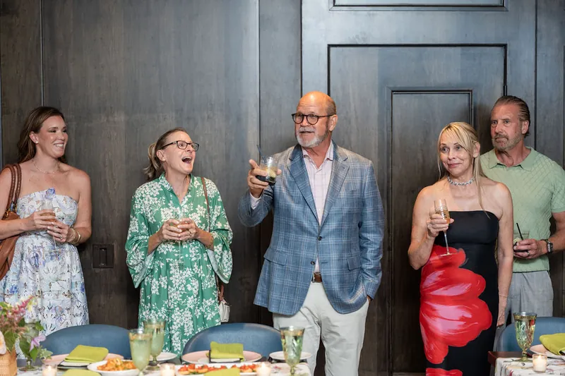 Five guests stand together at the bar area, holding drinks and smiling during the party.