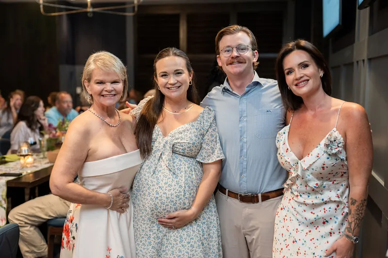Four guests pose as a group at the event, with one expecting a baby.
