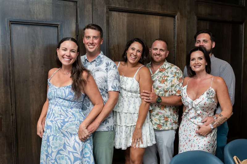 Six family members stand shoulder-to-shoulder in casual poses, dressed in patterned and solid-colored outfits in soft hues.