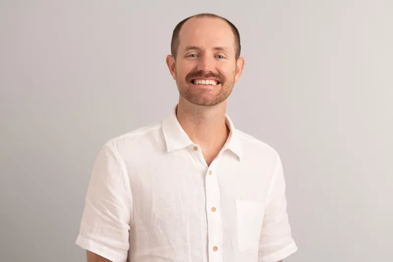 Man wearing crisp white button-up shirt with relaxed smile in studio setting.