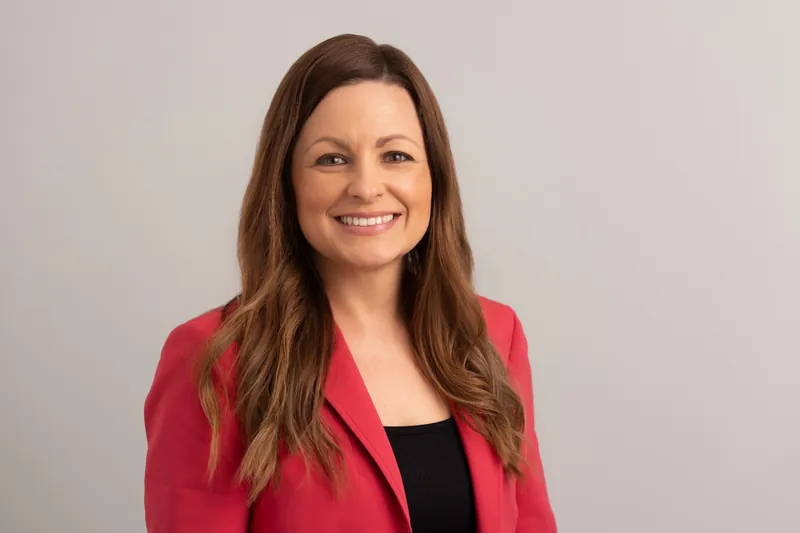Woman with long brown hair wearing a fuchsia blazer and black top, smiling directly at the camera.