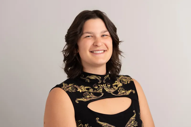 Woman in a black and gold floral cutout sleeveless top, smiling at the camera with her head tilted in the studio.